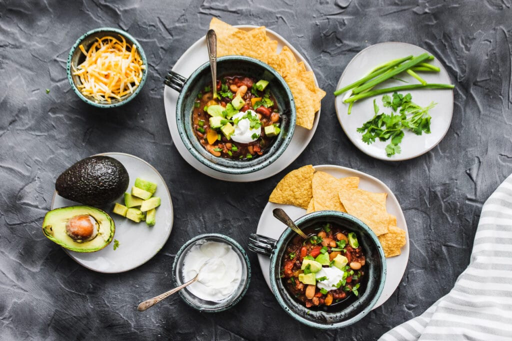 Sour cream, avocados, tortilla chips, and green onion shown with the chili. 