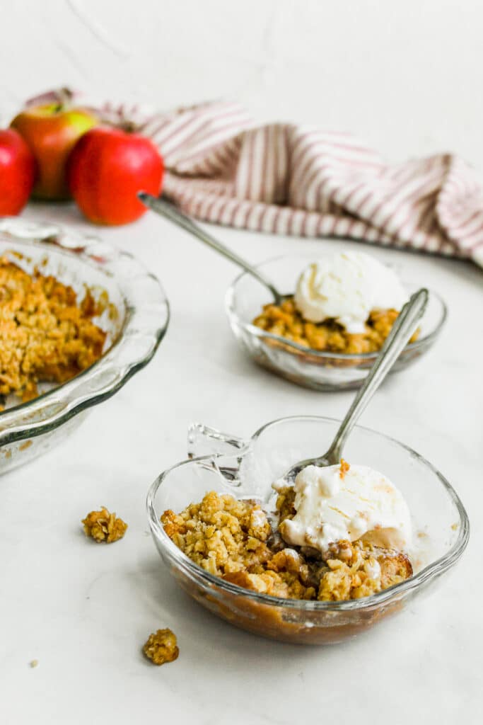 Bowl of apple crisp with oatmeal topping in an apple shaped bowl with ice cream.