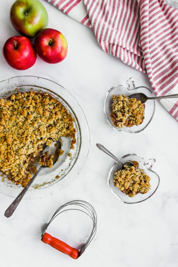 Looking at a pie plate full of apple crisp with some portioned into bowls.