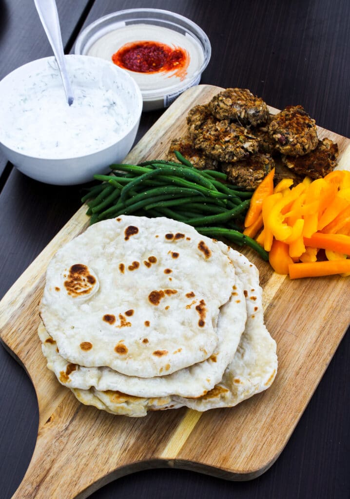 Stacked flatbreads alongside a tray of veggies, dips, and falafel.