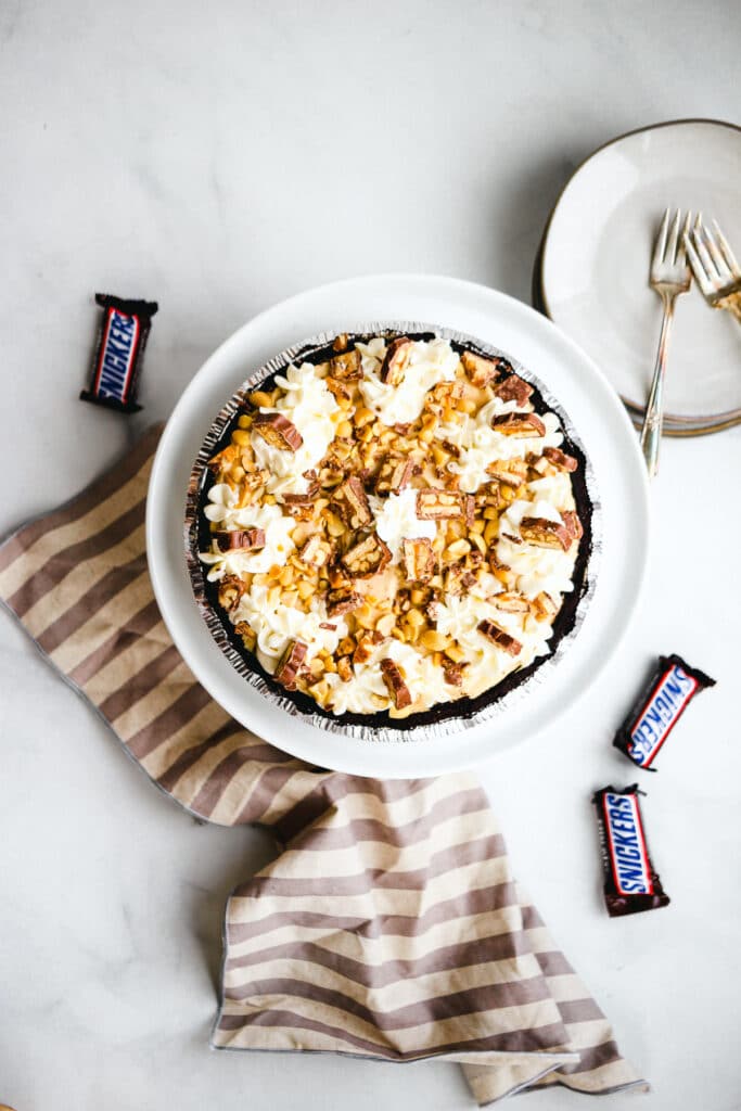 Overhead Snickers pie with whipped cream, Snickers, and peanuts.