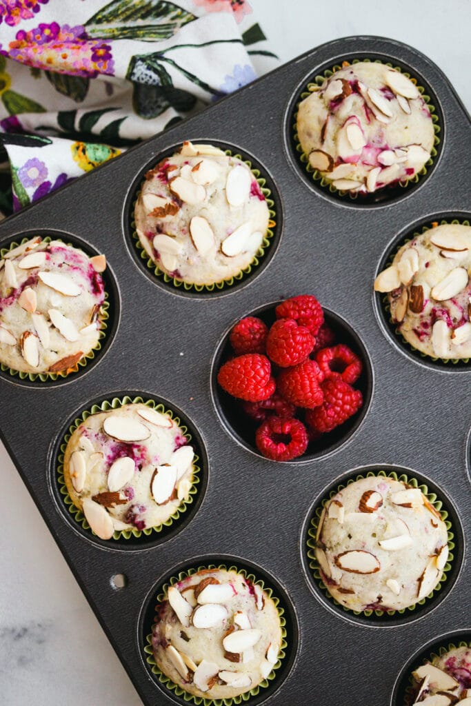 Muffin tin with baked muffins and raspberries.