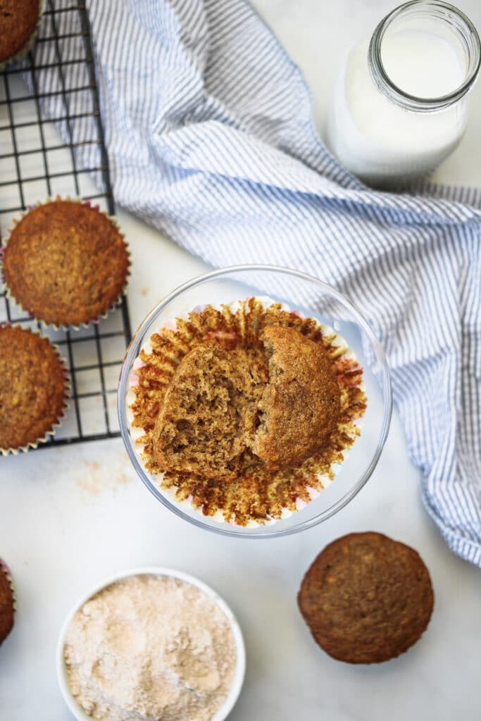 Cut open whole wheat banana muffin on a stand with milk and other muffins.