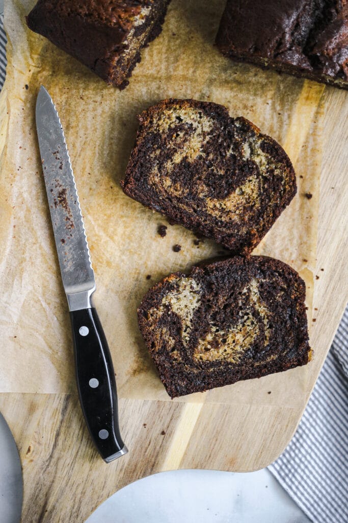 Two slices of chocolate swirl banana bread with a knife on a cutting board.