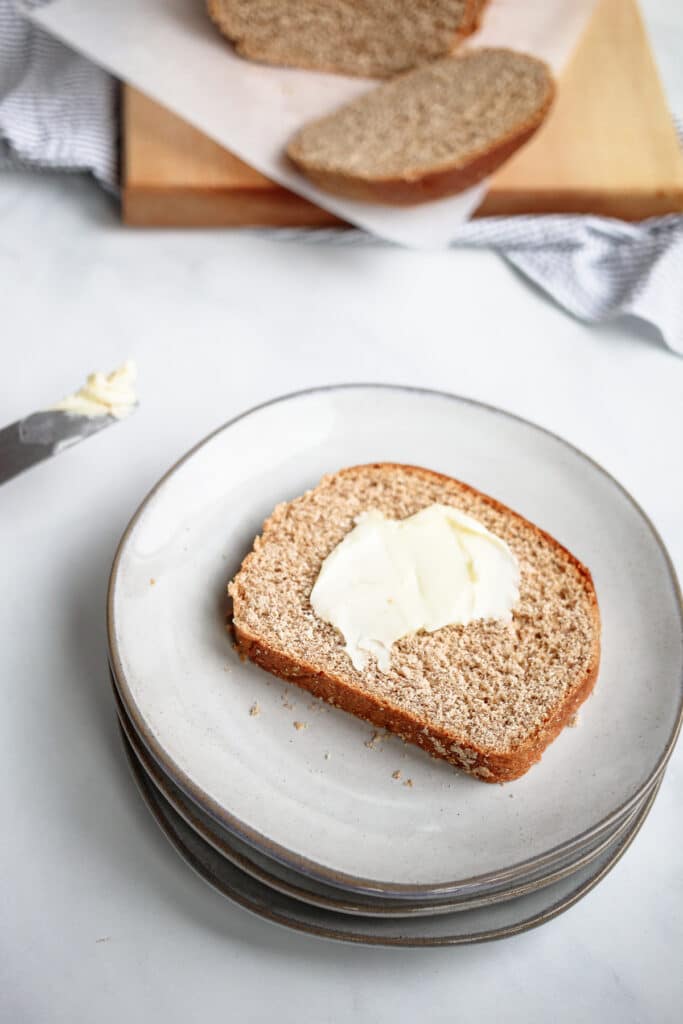 Slice of honey whole wheat bread on a plate with butter.