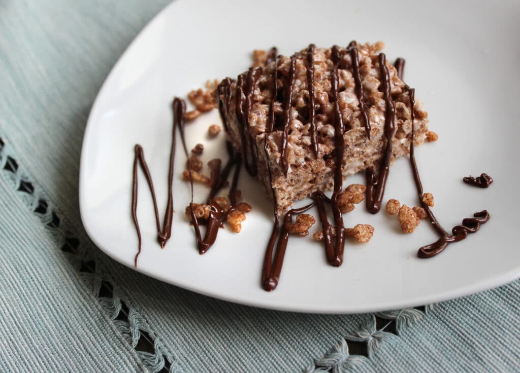 Chocolate krispie treat drizzled with chocolate on a plate.