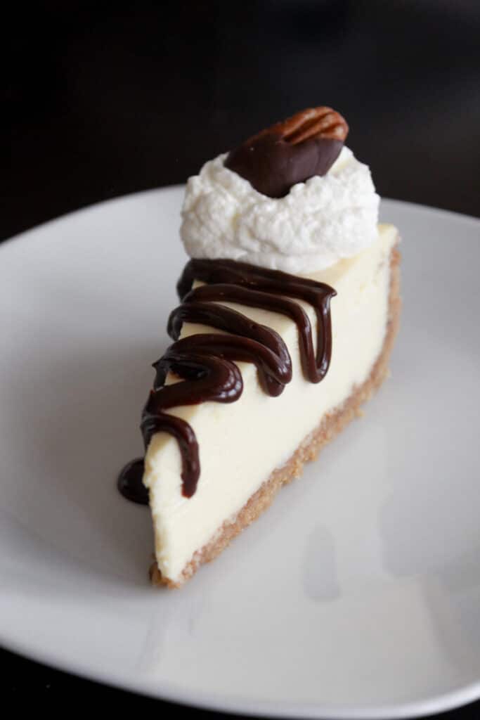 Slice of homemade cheesecake topped with chocolate sauce and whipped cream.