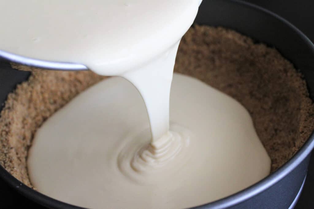 Pouring cheesecake filling into the crust.