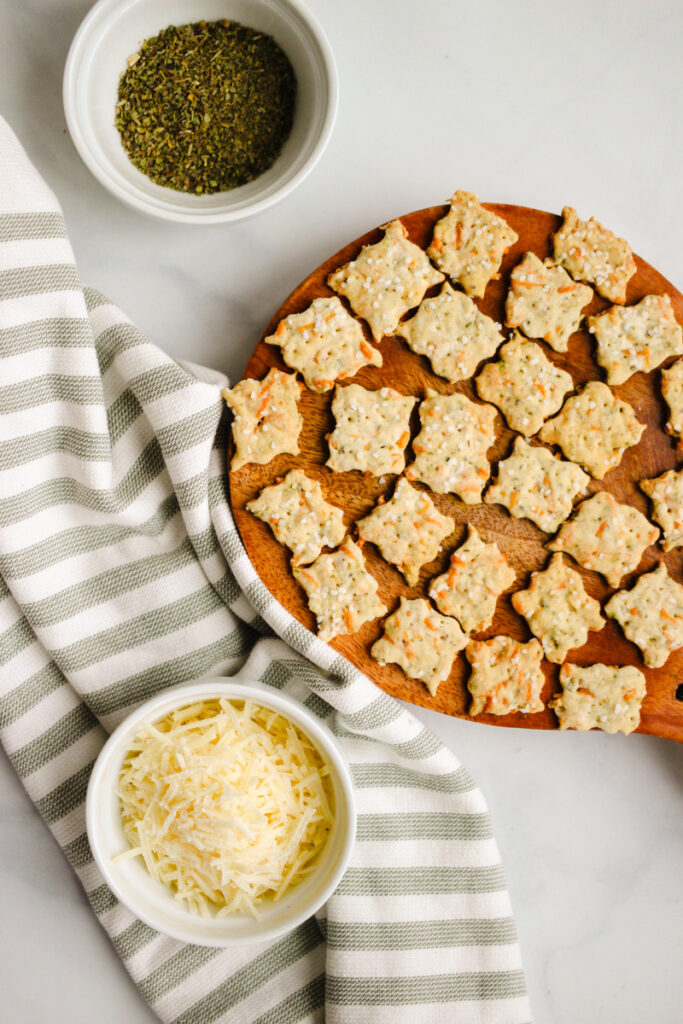 Crackers shown on wooden board with bowls of parmesan cheese and Italian seasoning.